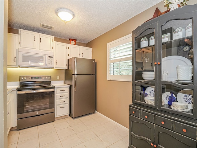 kitchen featuring appliances with stainless steel finishes, light tile patterned floors, a textured ceiling, and white cabinetry