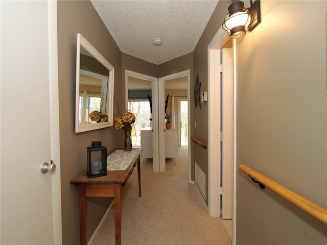 corridor with a textured ceiling and light colored carpet