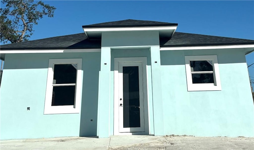 exterior space featuring a shingled roof and stucco siding