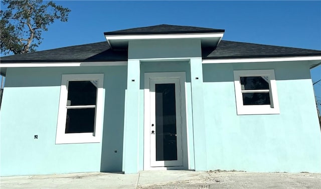 exterior space featuring a shingled roof and stucco siding