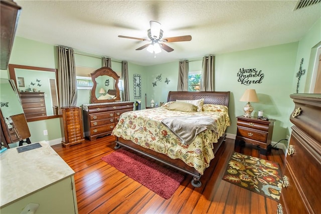 bedroom with a textured ceiling, dark wood-style flooring, visible vents, and a ceiling fan