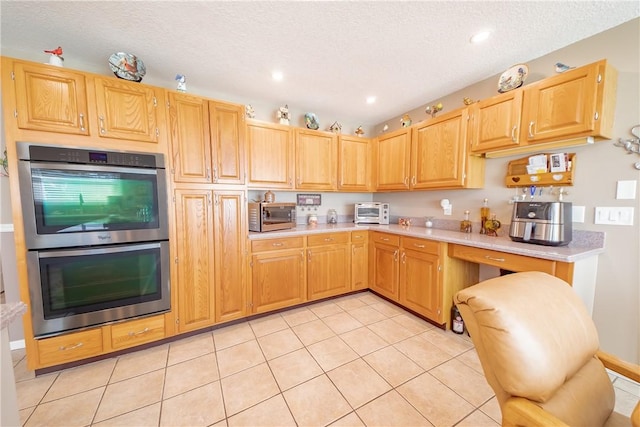 kitchen with double oven, light countertops, a textured ceiling, and light tile patterned flooring