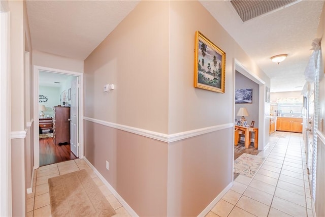 hall featuring light tile patterned floors, baseboards, and visible vents