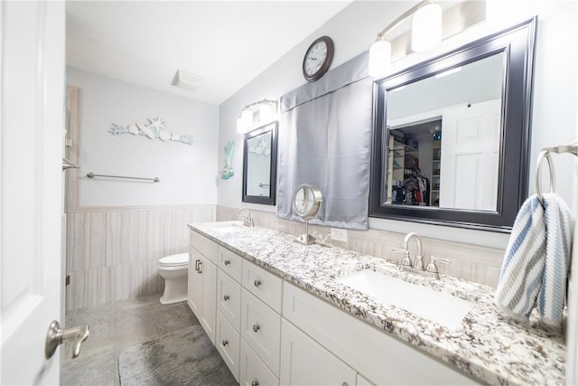 full bath with double vanity, a wainscoted wall, toilet, and a sink