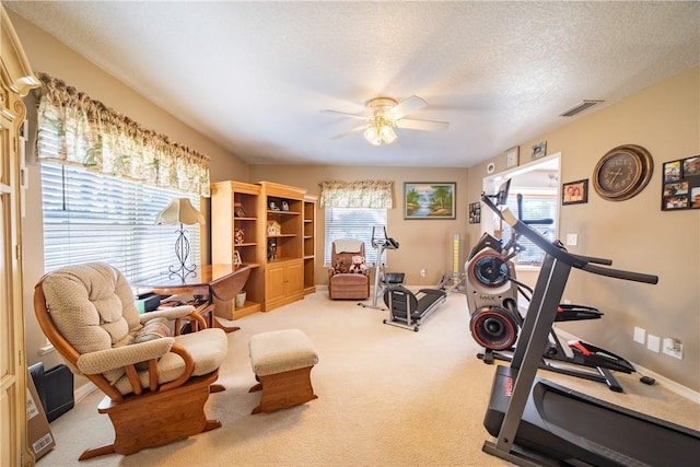 exercise area with a textured ceiling, light carpet, visible vents, baseboards, and a ceiling fan