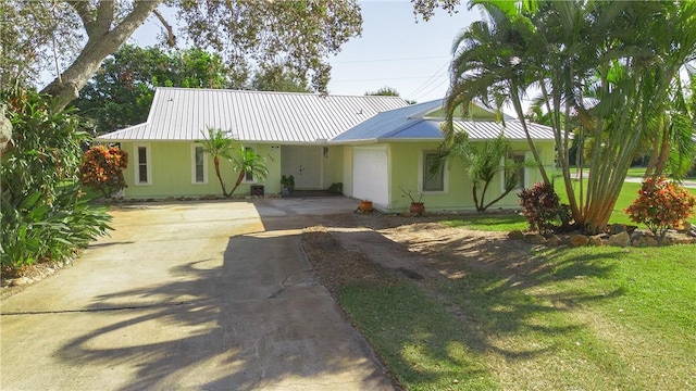 ranch-style house featuring a garage, driveway, metal roof, and a front yard