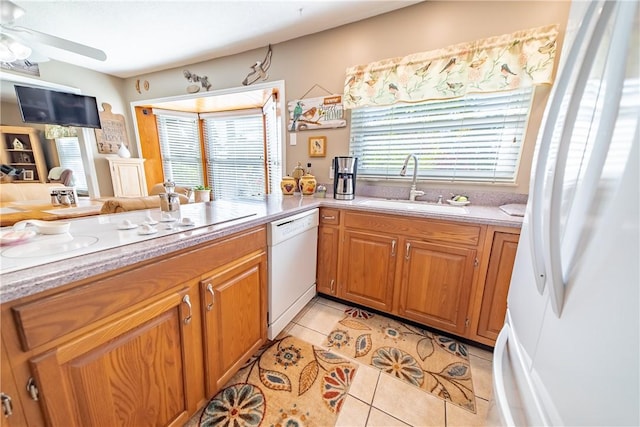 kitchen featuring light tile patterned floors, light countertops, brown cabinetry, a sink, and white appliances