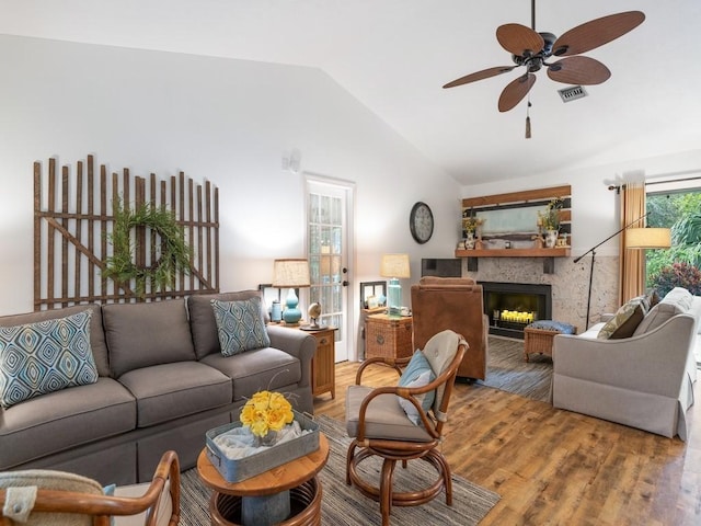 living area featuring visible vents, a ceiling fan, wood finished floors, vaulted ceiling, and a fireplace