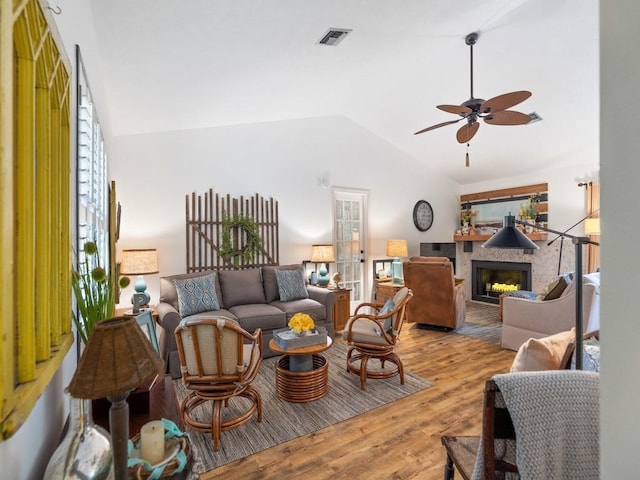 living area with ceiling fan, a fireplace, visible vents, light wood-style floors, and vaulted ceiling