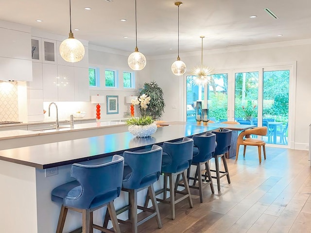 kitchen with backsplash, ornamental molding, white cabinets, a breakfast bar, and sink