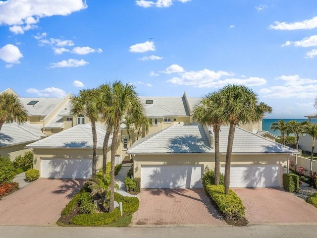 view of front of house with a garage, a tile roof, a water view, decorative driveway, and stucco siding