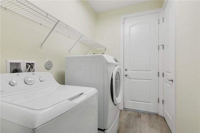 clothes washing area with independent washer and dryer and light hardwood / wood-style flooring