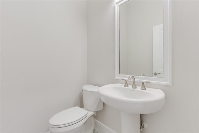 half bathroom with baseboards, a sink, and toilet