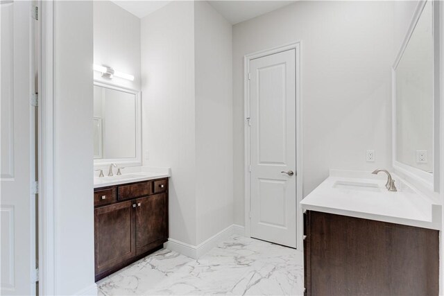 full bathroom featuring marble finish floor, baseboards, two vanities, and a sink