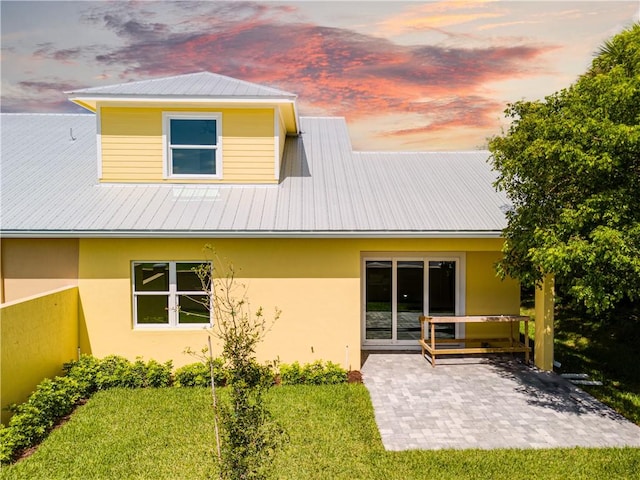 rear view of property featuring metal roof, a patio, a lawn, and stucco siding