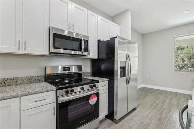 kitchen featuring stainless steel appliances, white cabinetry, light stone counters, and baseboards