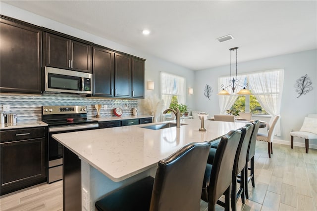 kitchen featuring sink, dark brown cabinets, stainless steel appliances, a center island with sink, and decorative light fixtures