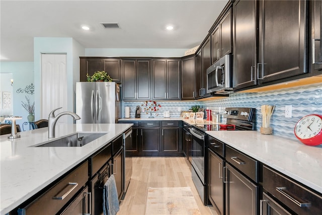 kitchen with sink, appliances with stainless steel finishes, dark brown cabinets, tasteful backsplash, and light wood-type flooring