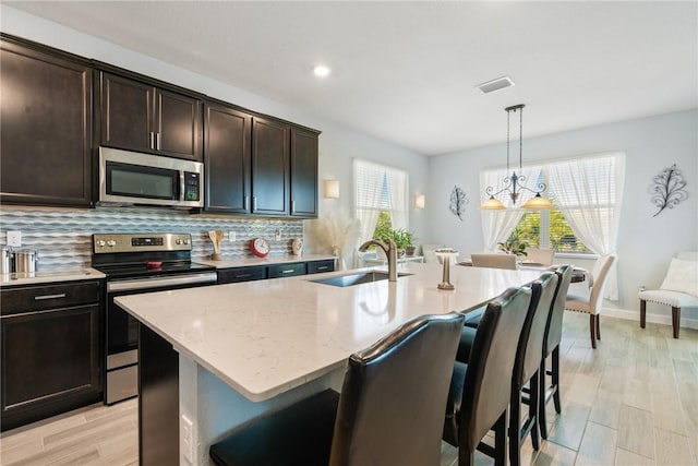 5990 Bearberry Dr, Vero Beach, FL 32967 - kitchen featuring stainless steel appliances, a sink, a breakfast bar area, backsplash, and an island with sink
