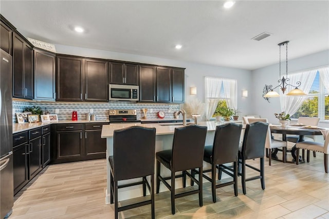 kitchen featuring dark brown cabinetry, sink, hanging light fixtures, stainless steel appliances, and a kitchen island with sink