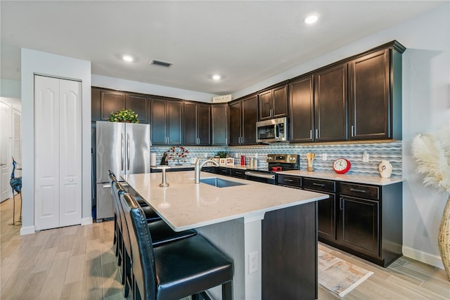 kitchen featuring stainless steel appliances, an island with sink, sink, and dark brown cabinetry