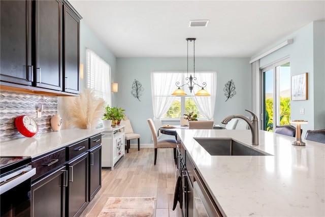 kitchen with pendant lighting, sink, light hardwood / wood-style flooring, backsplash, and light stone counters