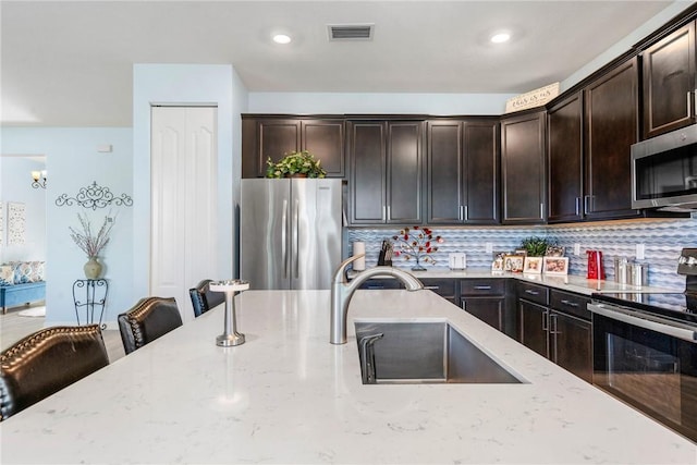 5990 Bearberry Dr, Vero Beach, FL 32967 - kitchen with appliances with stainless steel finishes, a sink, light stone countertops, backsplash, and dark brown cabinets