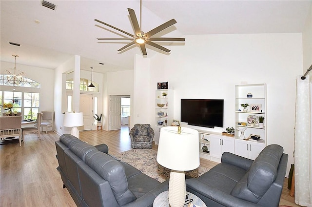 living room with ceiling fan with notable chandelier, built in features, high vaulted ceiling, and light wood-type flooring