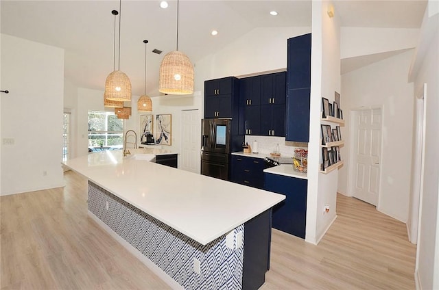 kitchen with high vaulted ceiling, decorative light fixtures, stainless steel fridge, a large island, and light hardwood / wood-style flooring