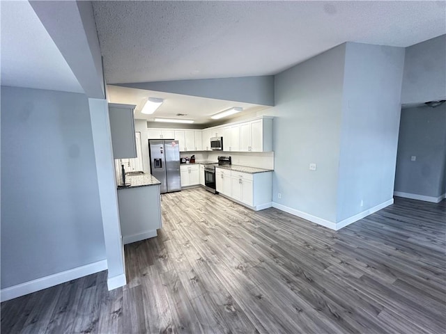 kitchen featuring appliances with stainless steel finishes, white cabinetry, lofted ceiling, light wood-type flooring, and a textured ceiling