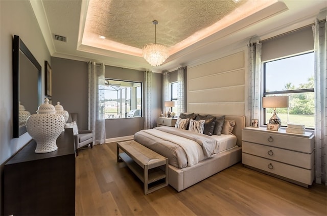 bedroom featuring wood-type flooring, a notable chandelier, and a tray ceiling