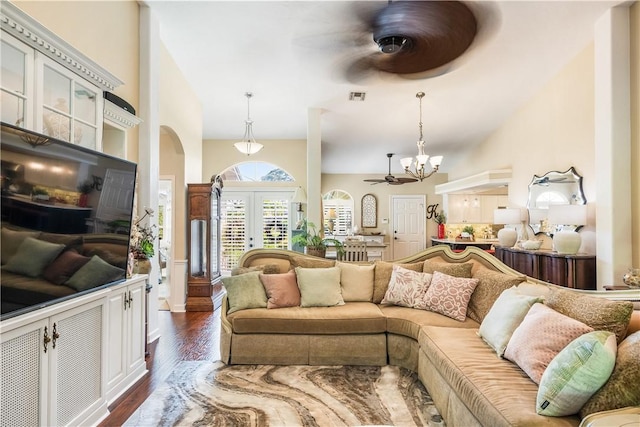 living room with a towering ceiling, an inviting chandelier, dark hardwood / wood-style flooring, and french doors