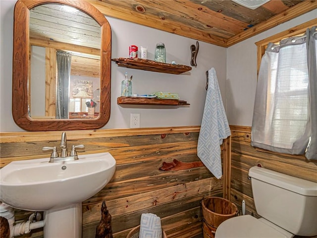 half bathroom featuring wooden walls, wood ceiling, toilet, wainscoting, and a sink