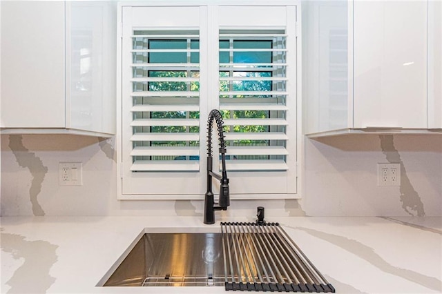 interior details with white cabinetry, a sink, and light stone countertops