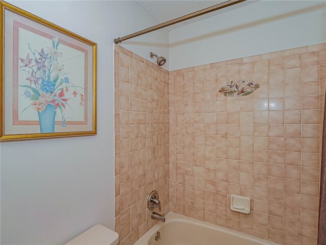 bathroom with a textured ceiling, tiled shower / bath combo, and toilet