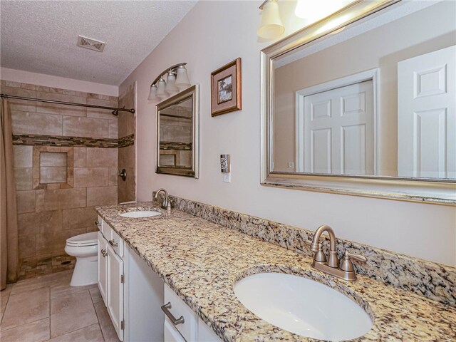 bathroom featuring tiled shower, toilet, tile patterned flooring, a textured ceiling, and vanity