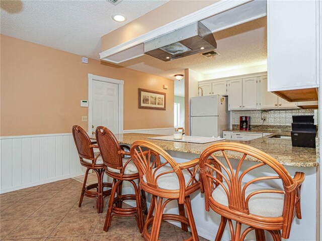 kitchen featuring light tile patterned flooring, a textured ceiling, white refrigerator, and kitchen peninsula