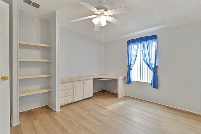 unfurnished office featuring built in desk, a textured ceiling, ceiling fan, and light wood-type flooring