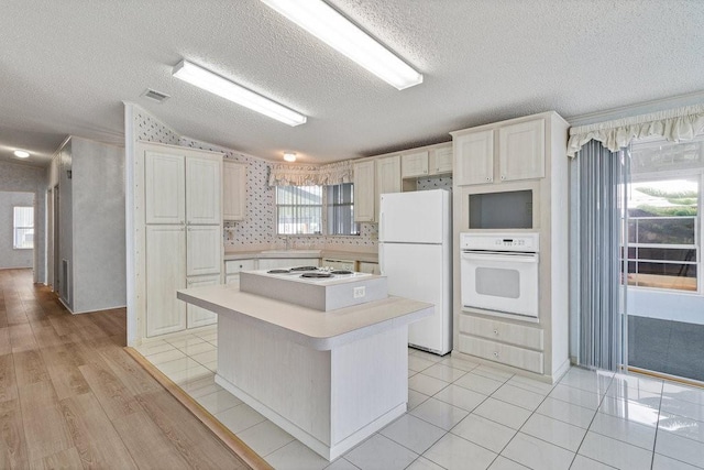 kitchen with white appliances, a center island, light tile patterned flooring, and a textured ceiling