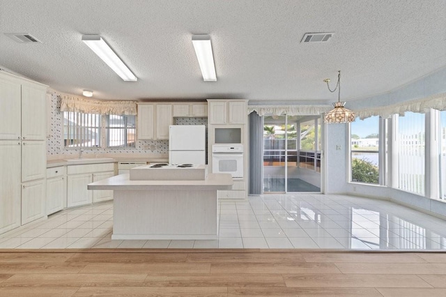 kitchen featuring white appliances, decorative light fixtures, light tile patterned floors, a kitchen island, and sink