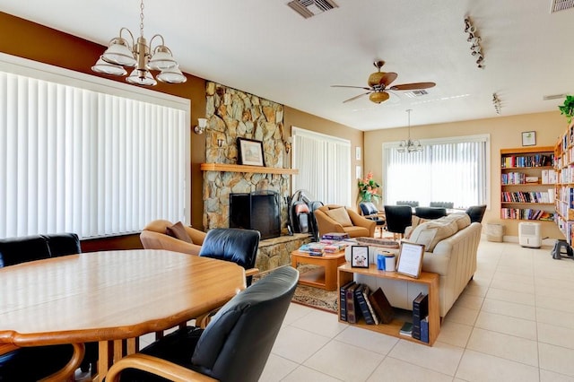 living room with ceiling fan with notable chandelier, rail lighting, light tile patterned floors, and a stone fireplace