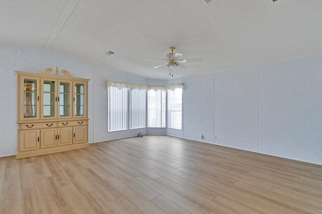 spare room featuring lofted ceiling, a textured ceiling, ceiling fan, and light hardwood / wood-style flooring