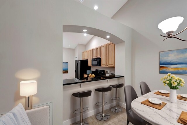 kitchen featuring lofted ceiling, black appliances, light tile patterned floors, a kitchen breakfast bar, and light brown cabinets