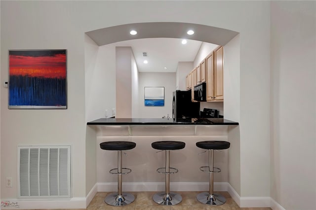 kitchen with a kitchen bar, black appliances, light tile patterned flooring, and light brown cabinetry