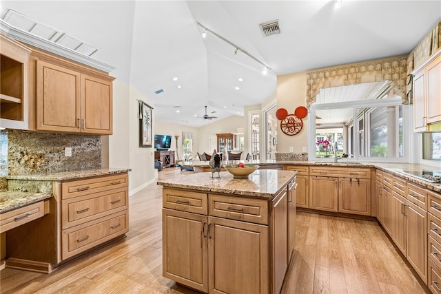 kitchen featuring light stone countertops, light wood-type flooring, backsplash, vaulted ceiling, and ceiling fan