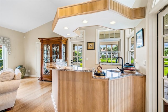 kitchen featuring vaulted ceiling, light stone counters, sink, and light hardwood / wood-style flooring