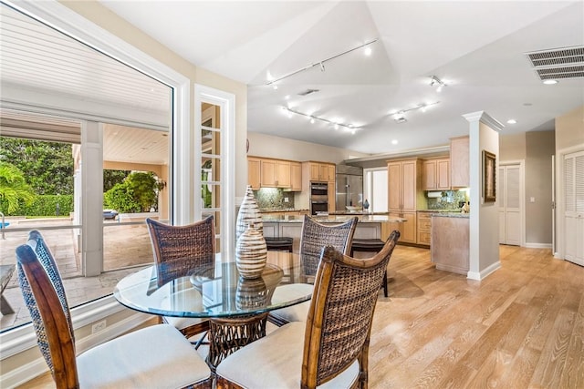 dining space featuring light hardwood / wood-style floors, lofted ceiling, and ornate columns