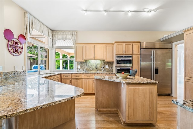 kitchen with tasteful backsplash, light stone counters, stainless steel appliances, sink, and light hardwood / wood-style floors