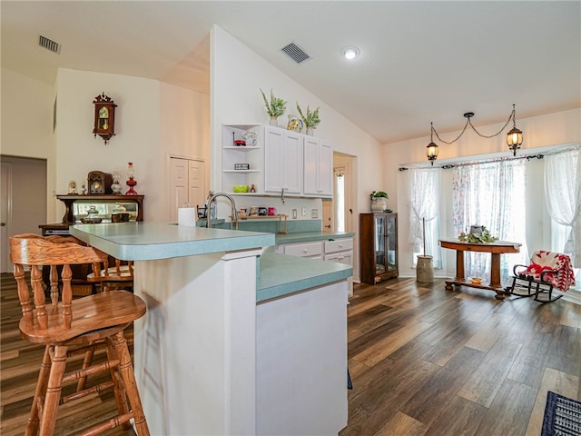 kitchen with white cabinetry, a breakfast bar, an island with sink, dark wood-type flooring, and vaulted ceiling