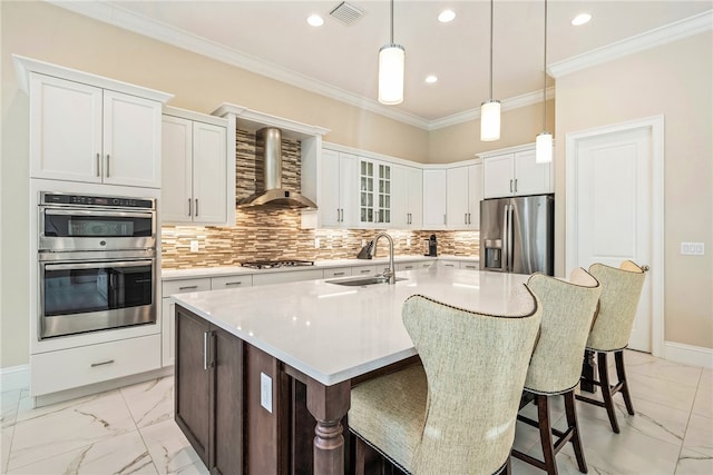 kitchen featuring sink, wall chimney exhaust hood, stainless steel appliances, a kitchen island with sink, and white cabinets